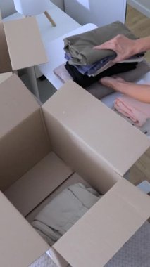 Kadın, geri dönüşüm ve bağış için karton kutuya kıyafet koyuyor. Yüksek kalite dikey 4k görüntü