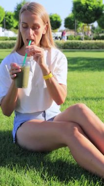 Çimlerin üzerinde buzlu kibrit çayı içen kadın. Yüksek kalite dikey 4k görüntü