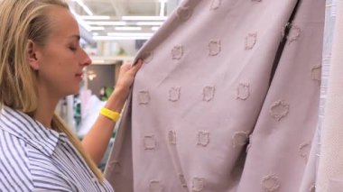 Kadın kumaş perdesini ev eşyaları mağazasında inceliyor, kumaşı ve dokuyu hissediyor. İç alışveriş kavramı, ev tekstili ve modern mobilyalar şık ve rahat ev tasarımı..