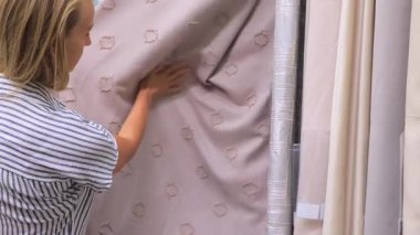 Kadın bir ev eşyaları mağazasında perde kumaşını inceliyor, dokunaklı doku ve malzeme kalitesi. İç alışveriş, tekstil seçimi ve modern ev dekorasyonu konsepti şık ve rahat tasarım için.