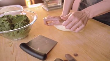 Çalışma masasının 4 km yavaş çekimde geleneksel İtalyan tarifi tortelli ya da yeşil ravioli içerikli hali. Uzman ev hanımı folyodan mangırı çıkarıyor ve elleriyle hamur topluyor.