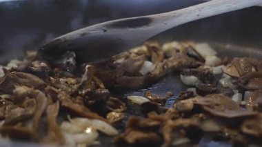 Ahşap bir kaşık porcini mantarı sotelenmiş soğanla karıştırır, zengin bir Akdeniz sosunda lezzetleri harmanlar. 4K yavaş çekim (120 fps,% 20 yavaşlatılmış), 45 açılı yakın çekim makro