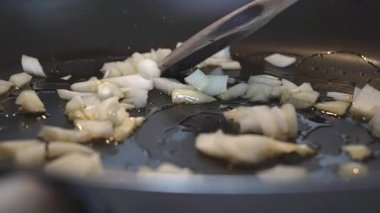 Bir ahşap kaşık zeytinyağında cızırdayan soğanları karıştırır. 4K yavaş çekim (120 fps,% 20 yavaşlatılmış) ile çekilen 45 açılı makro çekim, otantik İtalyan porcini mantarlı tagliatelle tarifinin ilk adımını gösteriyor.