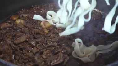 Taze pişmiş, dumanı tüten tagliatelle tavaya düşer ve zengin porcini mantar sosuyla karışmaya hazırdır. 4K yavaş çekim (120 fps,% 20 yavaşlatılmış), 45 açılı yakın çekim makro