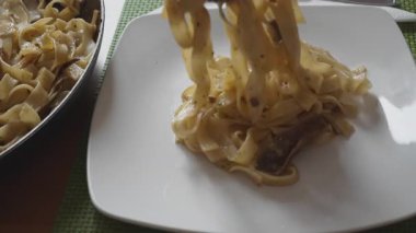Çatal, tavadan buharda pişen porcini mantarlı tagliatelle kaldırarak bir tabağa aktarıyor. 45 derecelik açıyla yakın çekim, 4K yavaş çekim (120 fps,% 20 yavaşlatılmış))