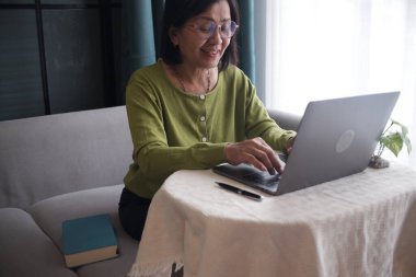 Evde dizüstü bilgisayar kullanan, kanepede yalnız oturan son sınıf kadınları..