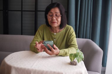 Evde telefon kullanan, kanepede yalnız oturan son sınıf kadınları.