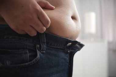 Beyaz odanın arka planında şişman kel adamın göbeği var..