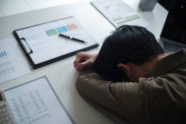 Çok çalışan stresli iş adamının ofiste çalışırken baş ağrısı olur, başını çalışma masasına koyar..