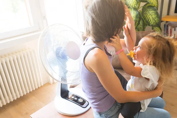 ペースメーカー付きの子供は母親の髪を使います彼らがリビングルームで冷めるファンに興奮しています 暑い夏の日に家のゲーム — ストック写真