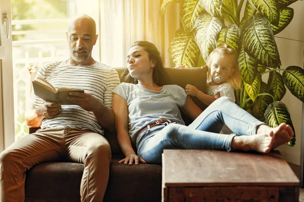 Dad reads to daughter and mom, little family on the sofa, enveloped in warm sunlight in the living room, comfortable family lifestyle