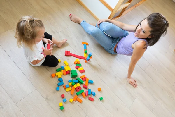 In a bright, light-colored room, mother and daughter play with colorful wooden constructions, talking to each other as they build and invent