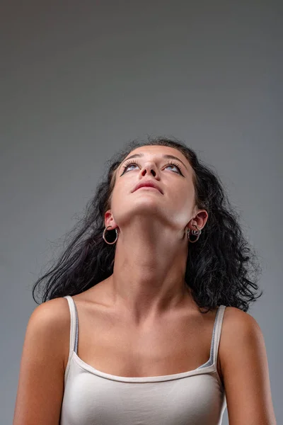 Frontal portrait of a young brunette girl in a tank top looking up by bending her head back and exposing the entire front of her neck