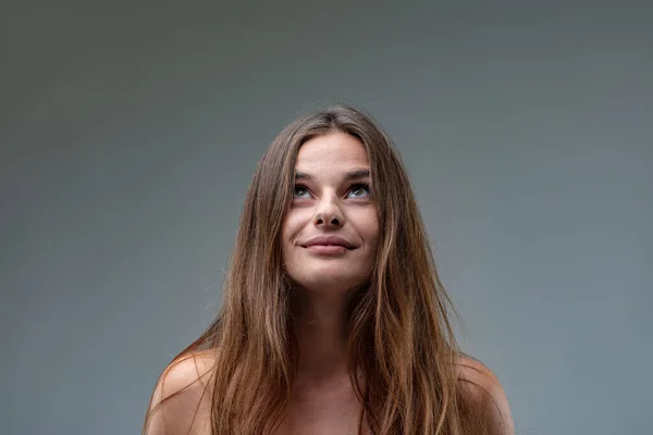 Frontal portrait of a young brown-haired young woman wearing a white sheath dress looking up because she sees something or because of her inventive