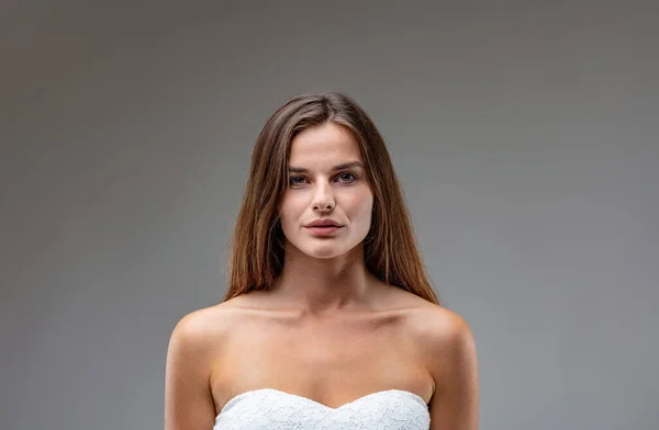 Central frontal portrait of charming and attractive young brown-haired woman wearing a white strapless dress. She conveys both the strength of beauty and youthful physique and that of willpower and in