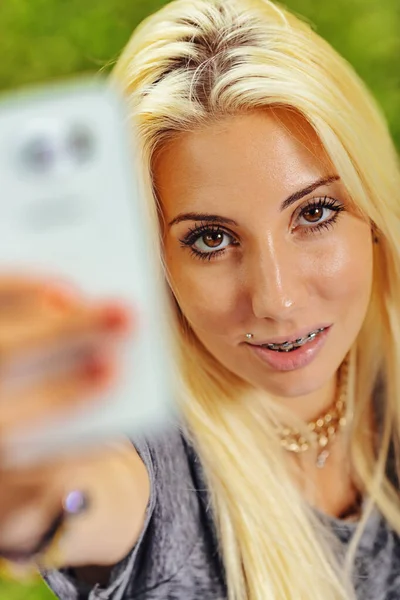 Vertical portrait of young blond woman in selfie position. Fixes the lens with intense eye-contact. She smiles highlighting her orthodontic braces that nonetheless make her even more attractive. Compl