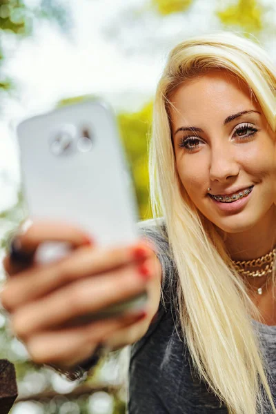 Красивая Блондинка Забавно Смотрит Свой Мобильный Телефон Улыбка Оставляет Зубы — стоковое фото