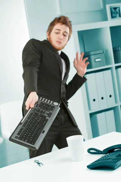 オフィスワーカーはキーボードで追いかけるバグに恐怖に苛まれる 彼は恐れているし ワイヤレスコンピュータのキーボードで若いビジネスマンを怖がらせるクモを追い払うしようとします — ストック写真