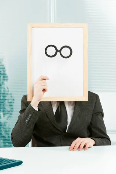 Man with framed sign head in an office. In front of the fake head made of signboard he also places cardboard glasses to complete a disguise that YOU can customize graphically.