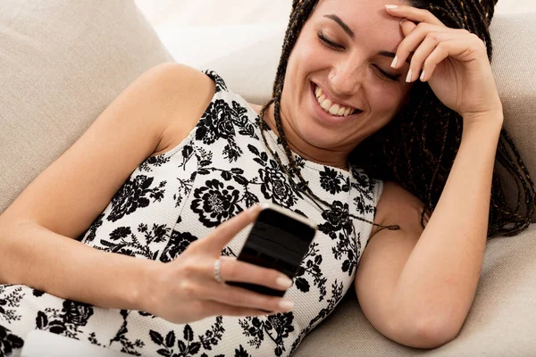 Ung Kvinna Med Box Flätor Liggande Soffan Med Sin Smartphone — Stockfoto