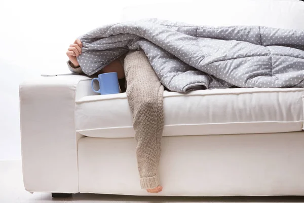 woman, lying on front, white couch, warm quilt, sweater, overwhelmed, flu, peeking, lifting fabric, weak arm, exhausted, hot tea, mug, sickness, illness, influenza, covered, rest, recovery, fatigue, t