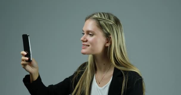 Genç Sarışın Kadın Akıllı Telefonu Tarafsız Bir Arkaplana Karşı Kullanıyor — Stok video