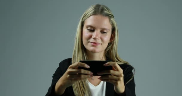 若いブロンドの女性は静かに中立的な背景にスマートフォンを使用しています インターネット接続が機能しなくなり 彼女はそれを粉砕したい — ストック動画