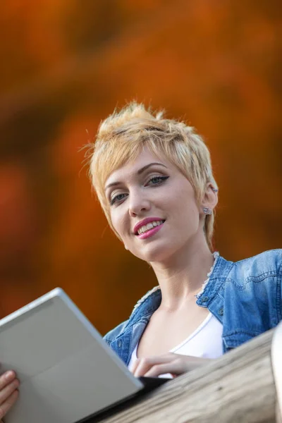 一个金发短发美女的户外肖像 穿着运动衫 手持数字平板电脑 骄傲地微笑着 从下面拍摄 在一个自然的高山环境与温暖 秋天科 — 图库照片