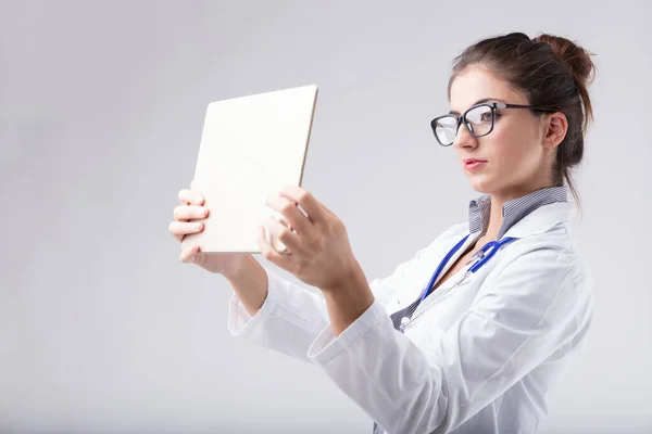 一名身穿白色实验室外套的妇女仔细检查了放在眼睛水平的数码平板电脑上的数据 好像它是一部X光片 这没有任何意义 但它让人想起了这个概念 — 图库照片