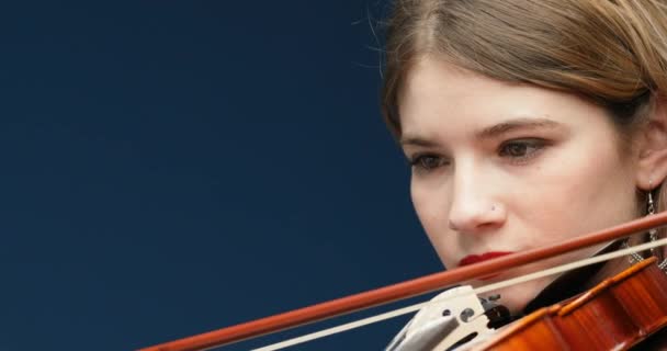 パノラマカメラの動きは 古典的な音楽家 弦楽器 赤塗りの爪を持つ手の詳細を明らかにします 若い女性が弓 ブロンドとフクシアの髪 鼻ピアス 肩の演奏会のドレスでバイオリンを演奏 専門職クラシックM — ストック動画