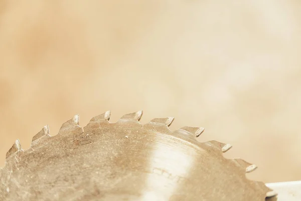 Close-up detail of half circle of toothed circular saw seen in profile in focus, while the rest of the carpenter\'s workshop is blurred behind.