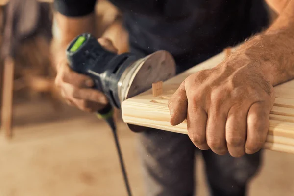 木匠的手抓住砂子 木匠是一位经验丰富的专业人员 他用强壮而精确的手握住木板或木片 用震动砂子的机器小心地将其磨砂 — 图库照片