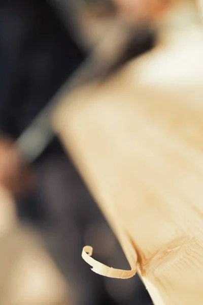 大工がドローナイフで作業しているボードにまだ取り付けられている木製のカールに焦点を当てた極端なクローズアップ 意図的に焦点を当てていない すぐにシェービングになりますが 今は美しいです — ストック写真