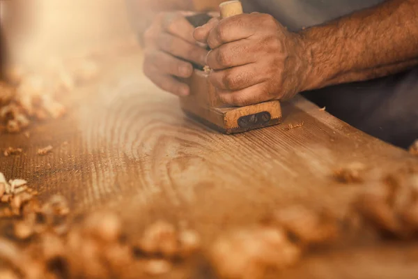 大工として知られる堅実で強い男である木工職人は 板を伝統的な方法で平面化し 金色の木のカールのように見えるおがくずの削り屑を作り出します それは骨の折れる — ストック写真