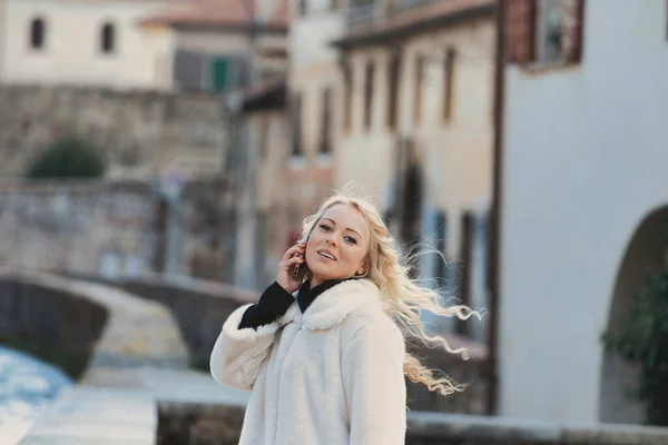 完全に実行ブロンドの髪 完璧なメイクとマニキュアを持つ若い女性は 中世の村とヨーロッパの都市の観光客です 彼女の携帯電話を使用して彼のために話す チャット またはアクセスするWi — ストック写真