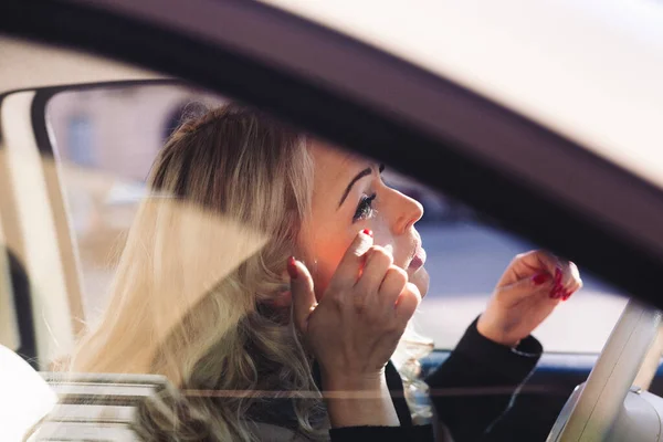 金髪の女性が化粧を触ったり 車に乗せたりしています 彼女は素晴らしいと自分自身と潜在的な日付のために完璧になりたいです今夜 獲物ではなくハンターだ — ストック写真