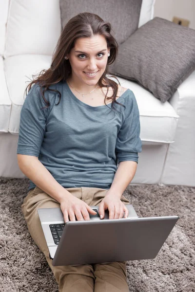彼女の家の柔らかく快適なカーペット上の若い女性は ラップトップコンピュータを使用しています 勉強してるのか楽しいのか すぐにインターネットに到達する無線Lanとブロードバンドのおかげで 彼女はありません — ストック写真