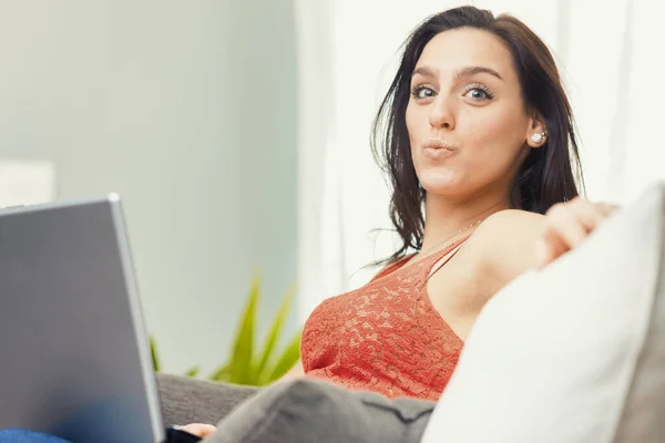 一个穿着红色花边背心的女人正忙着在家里用她的笔记本电脑 舒适地坐在沙发上 她能高效地工作 不受办公室环境压力的干扰 不是这个就是那个 — 图库照片