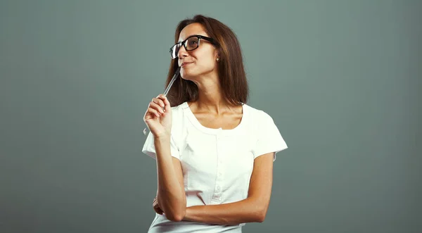 Young woman feeling an emotion, pondering on captivating ideas, pen in mouth, donning glasses, white shirt, attractive and slender