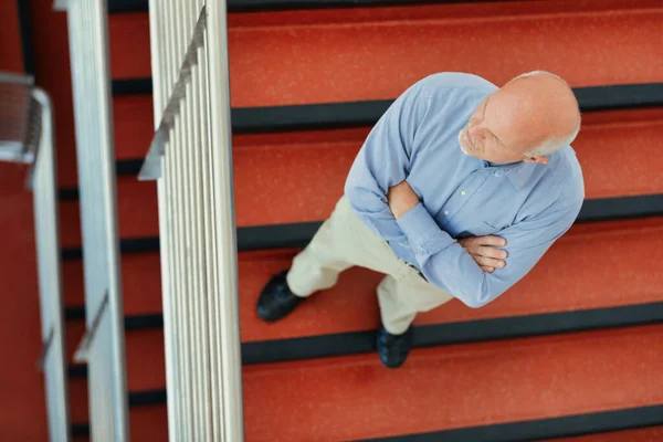 从上面看到一个手臂交叉的老人 他站在一个红色的楼梯上 望着远方 他是在为自己和心爱的人的安全着想呢 还是在为将来担心呢 — 图库照片