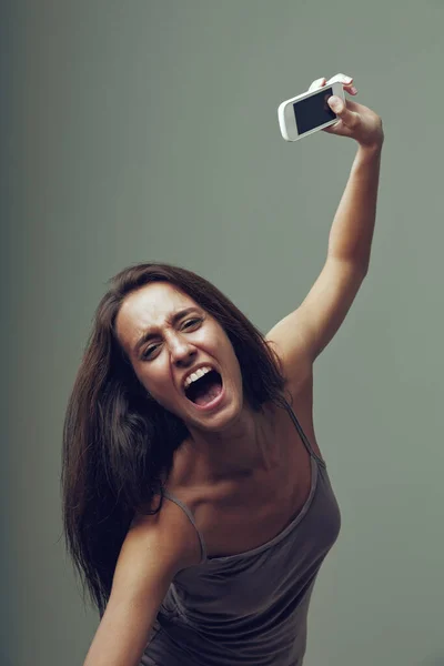 怒っている女の子は怒りで彼女の携帯電話を投げる 中立的な背景に孤立した若い女性の感情的な肖像画 彼女は 私はこのスマートフォンとインターネットにうんざりしている と考えています 悲鳴を上げながら — ストック写真