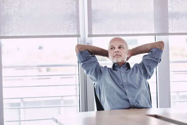 Man in office relaxes with arms crossed behind his head, dreaming of vacation, weekend or retirement