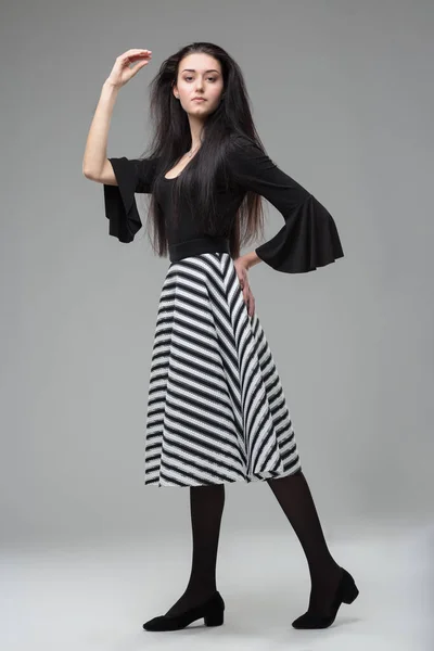 优雅的年轻女人 长长的黑头发 模型的白色连衣裙 斑马条纹鲱鱼裙 黑色长袜 高跟鞋 成熟的美 丰满的身材 灰色的背景 — 图库照片