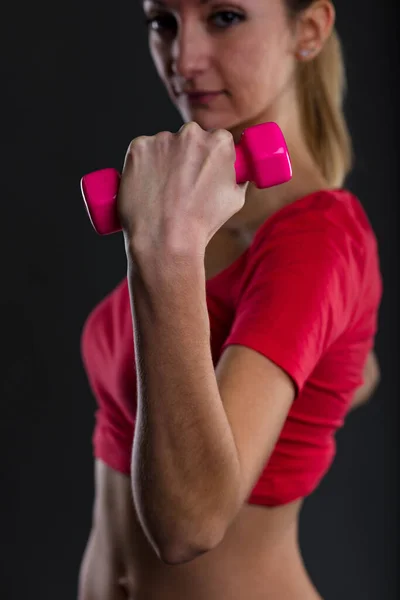 フィットネスの女性は 背景にぼやけてピンクの重量を持ち上げる 誇り高いブロンド 赤いトップ 達成目標を紹介します 平たい胃 株式会社佐野のメンズサナ 彼女のモットーです — ストック写真