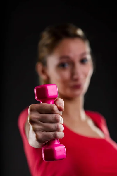フィットネスの女性は 背景にぼやけてピンクの重量を持ち上げる 誇り高いブロンド 赤いトップ 達成目標を紹介します 平たい胃 株式会社佐野のメンズサナ 彼女のモットーです — ストック写真