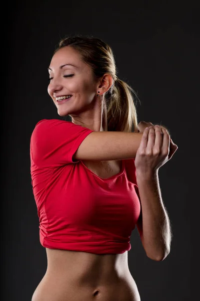 赤のトップと黒のミニパンツの幸せなトーンの女性は腕のストレッチを行います 彼女の平らな胃と筋肉は彼女の健康的なライフスタイルの証拠です — ストック写真