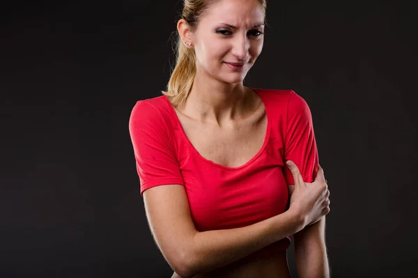 穿着红色衬衫的女人 表现出不适 面带微笑 紧紧抓住二头肌 厌倦了 厌倦了 可能是过度劳累的肌肉在健身房 褪色的黑色背景 — 图库照片