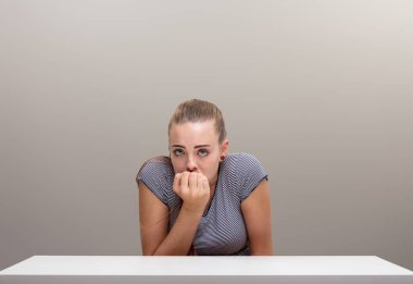 A girl, curled up, appearing small, frightened, defenceless, nibbles her nails, seeking help through her gaze. She confronts risk, fear, doubt, the unknown, and negativity at a table clipart