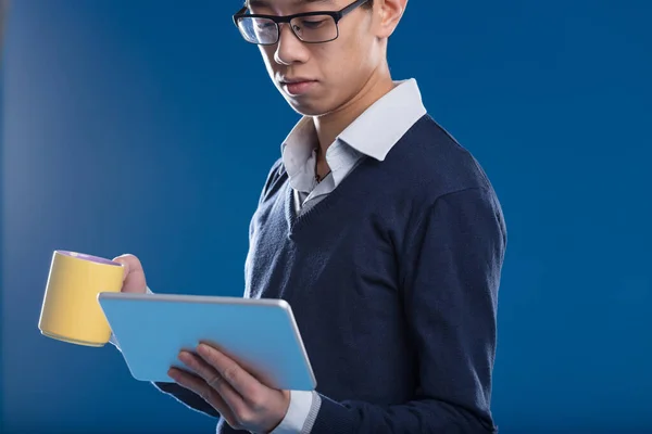 Asian Man Checks News His Tablet Holding Yellow Mug Blue — Stock Photo, Image