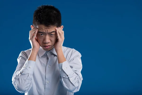 Young Asian man shows suffering, sadness. Is it a severe headache, a breakdown, or need for mental help? Maybe an economic or emotional loss? His expression signals negative, evident dismay
